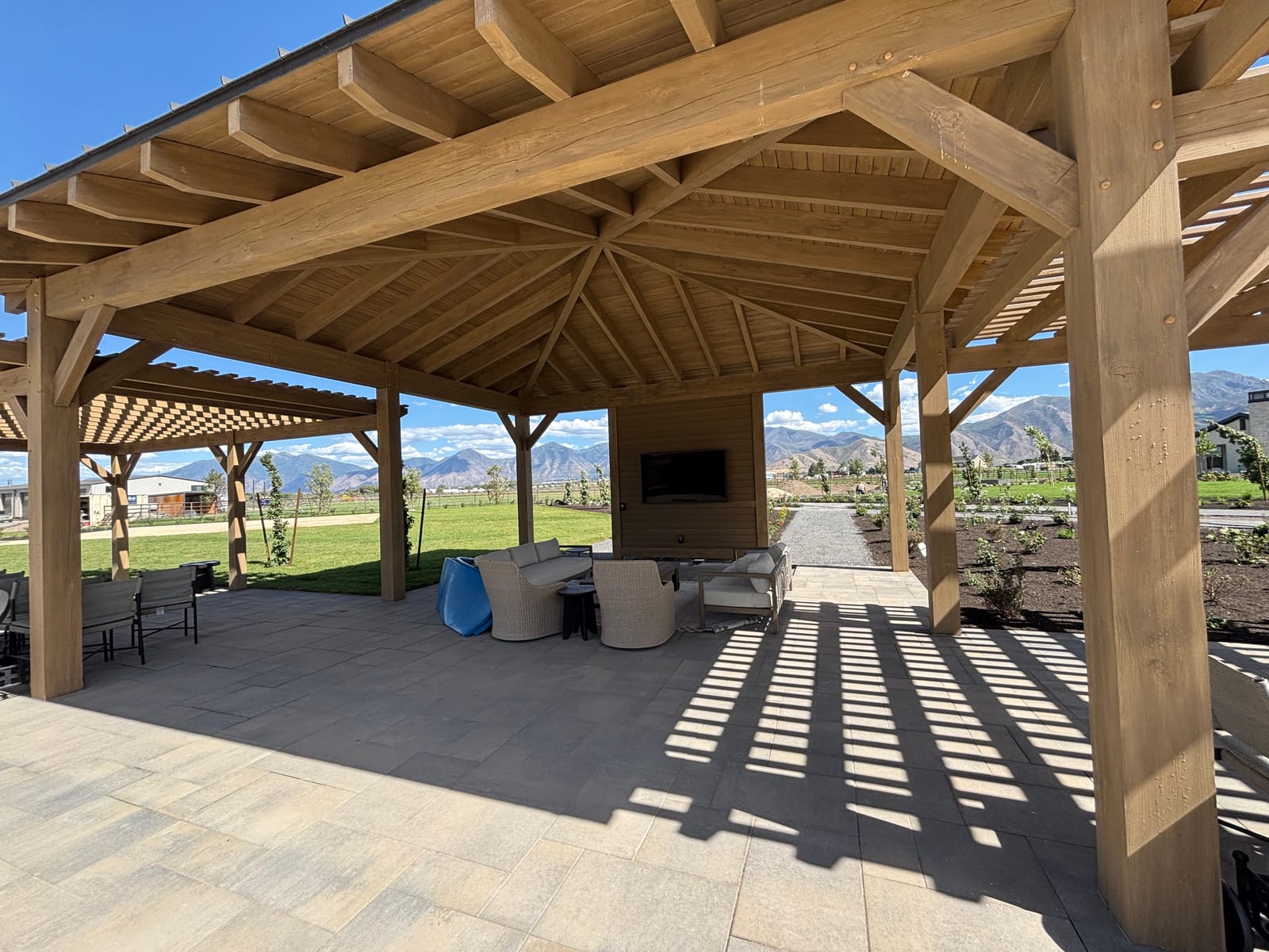 Open-air timber pavilion with exposed rafters over a paver patio lounge