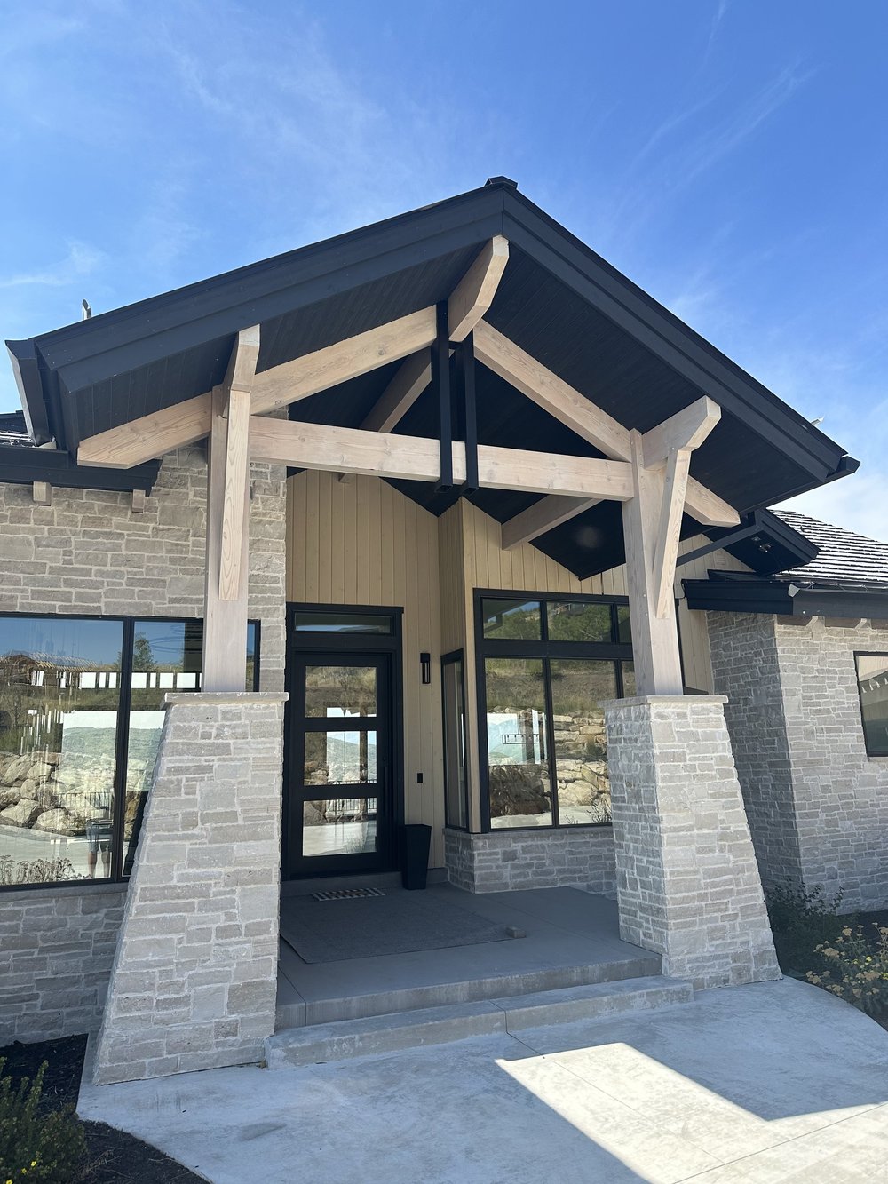 Front view of a modern house with timber beams on the exterior, and a covered porch pergola with heavy timber supports