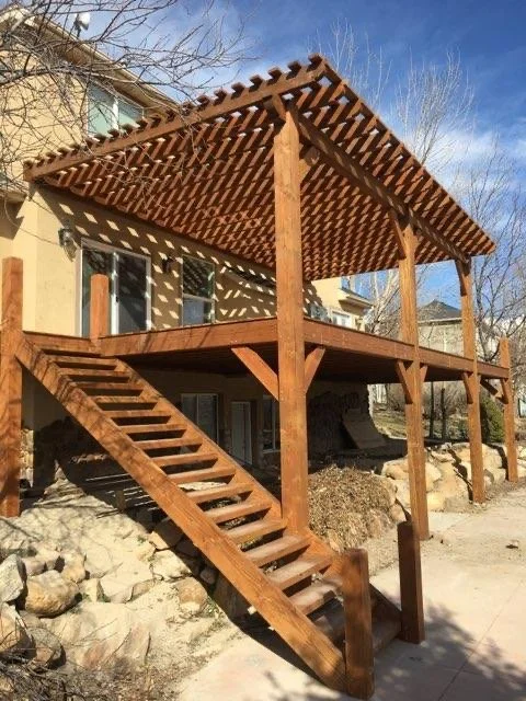 A timber deck with stairs leading up to the second-story balcony pergola, attached to a house